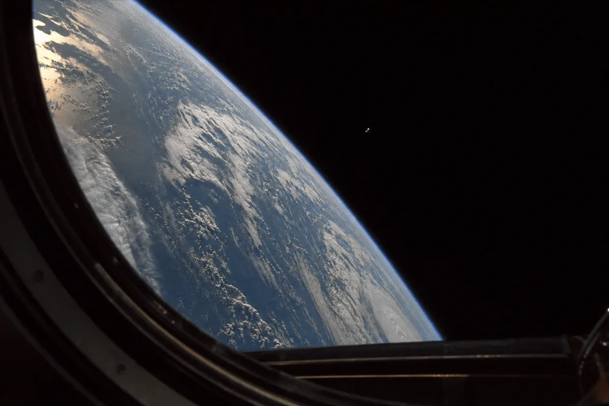 Limb de la Terre depuis l'orbite terrestre basse avec un objet non identifié visible près du centre-droit du cadre, esthétique de l'ère STS-80