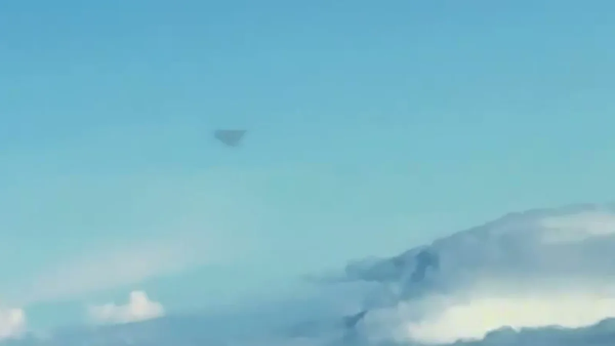 Dark triangular object above cloud deck from aircraft window