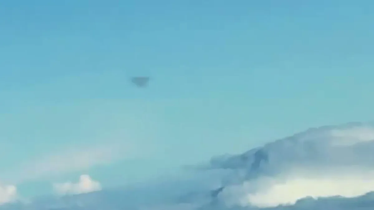 Dark triangular silhouette above a daytime cloud deck, filmed from a commercial aircraft window south of Carrollton, Georgia